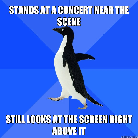 stands at a concert near the scene still looks at the screen right above it  Socially Awkward Penguin